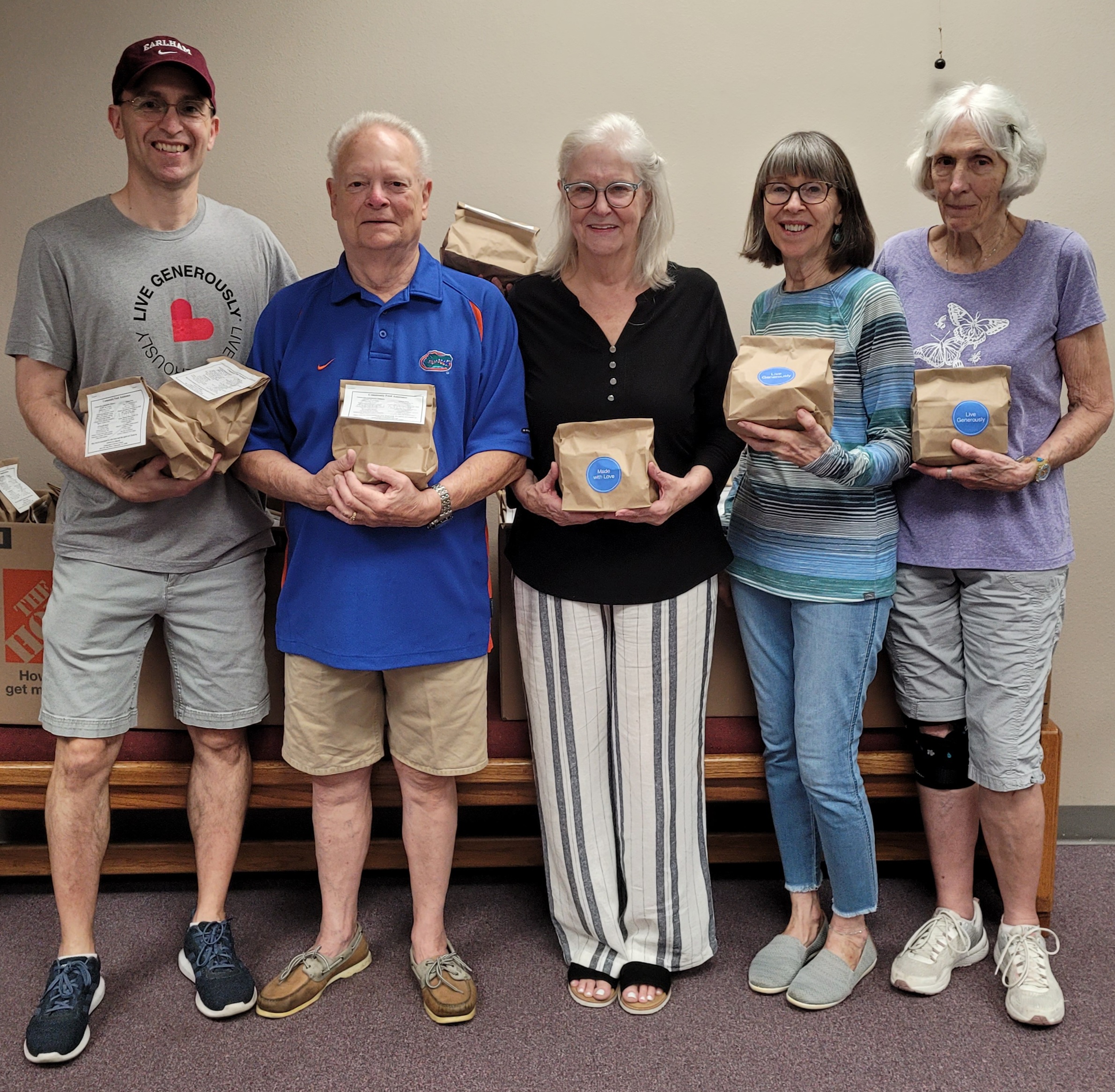 Five church members stand holding lunch sacks meant for the community.